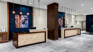 A reception area with two reception desks, a large abstract painting on the wall, and hanging pendant lights. - DoubleTree by Hilton Hotel Arlington DFW South (Arlington)