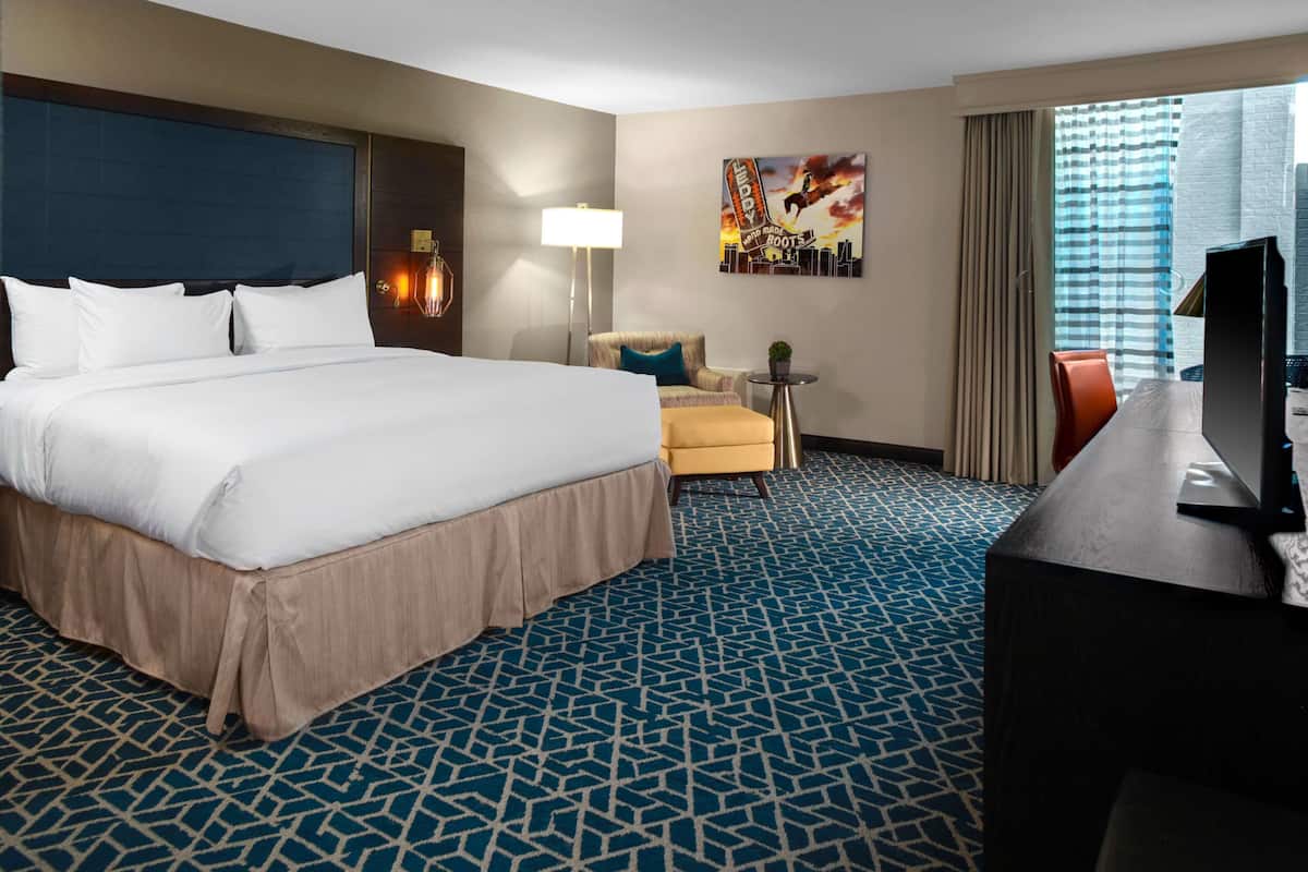 A hotel room with a large bed, a desk, a chair, a lamp, and a painting on the wall.