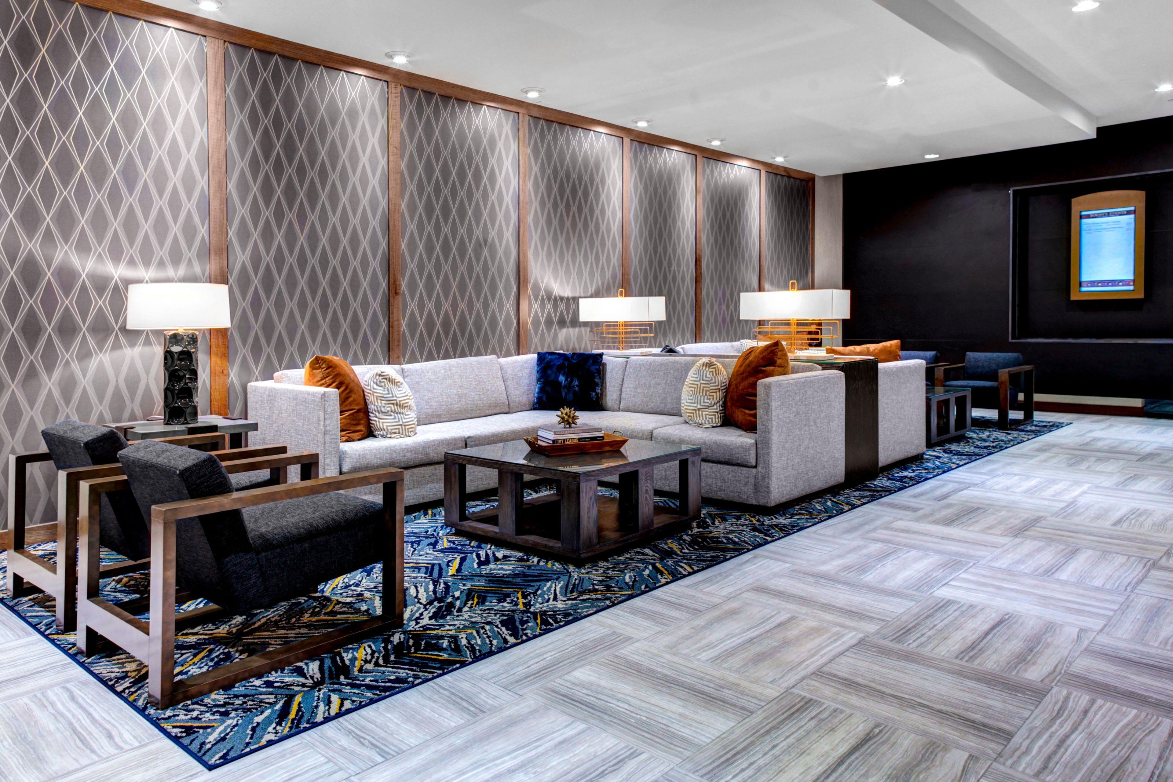 Un moderno vestíbulo de hotel con un sofá modular, sillones, una mesa de centro y una alfombra estampada.