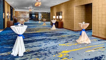 A hotel lobby with a blue and yellow carpet, round tables with white tablecloths tied with blue ribbons, and a wooden partition with a decorative bird hanging from the ceiling.