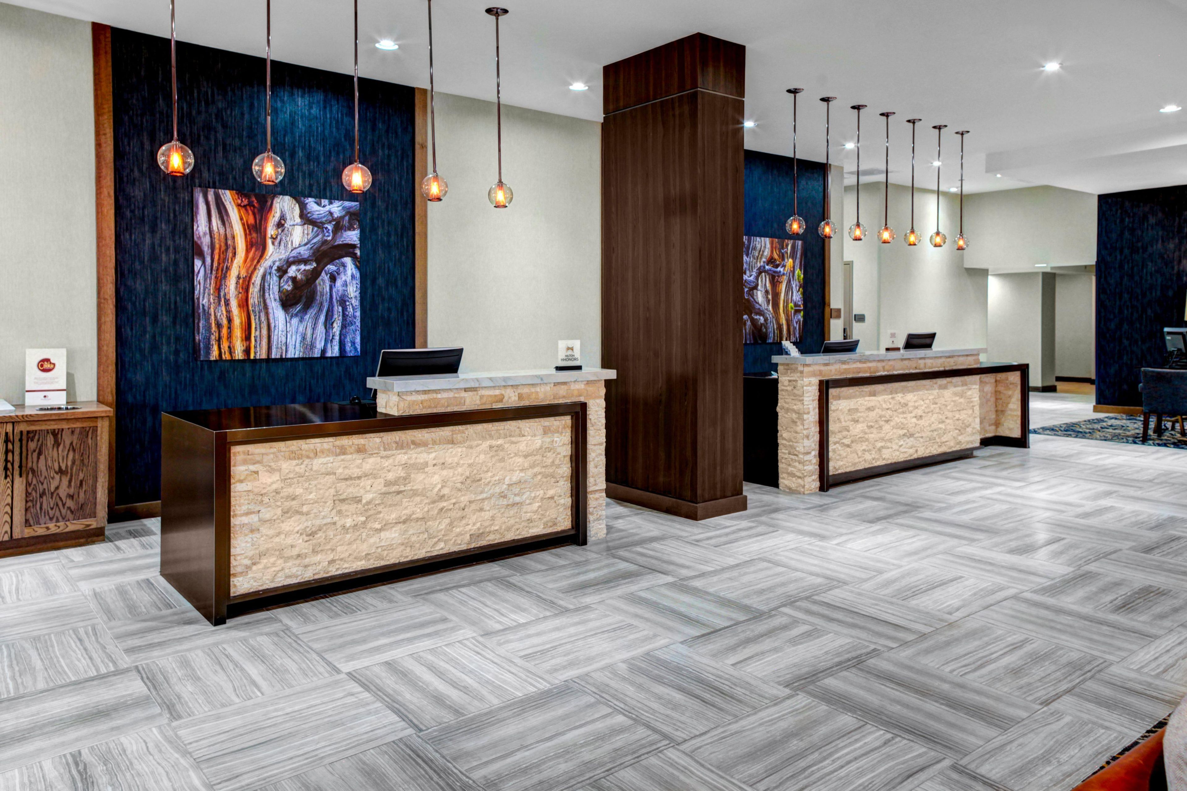 A hotel reception area with two reception desks, modern pendant lighting, and abstract wall art.