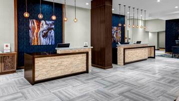 A hotel reception area with two reception desks, modern pendant lighting, and abstract wall art.