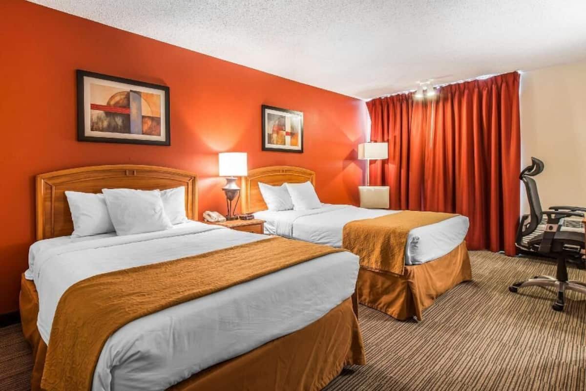 A hotel room with two beds, a desk, a chair, and two lamps.
