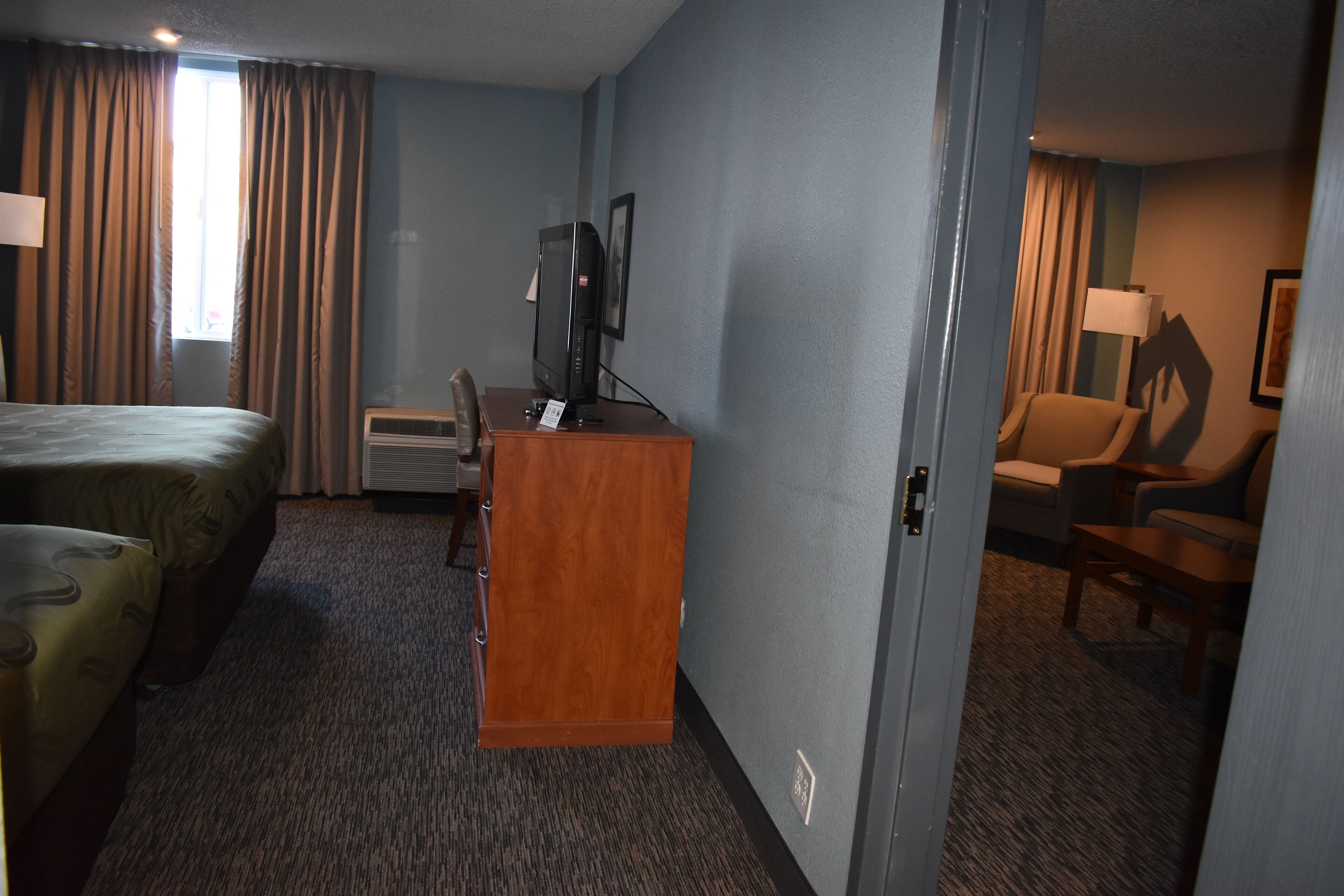 Una camera d'albergo con un letto, una scrivania con televisore, una sedia e una lampada.