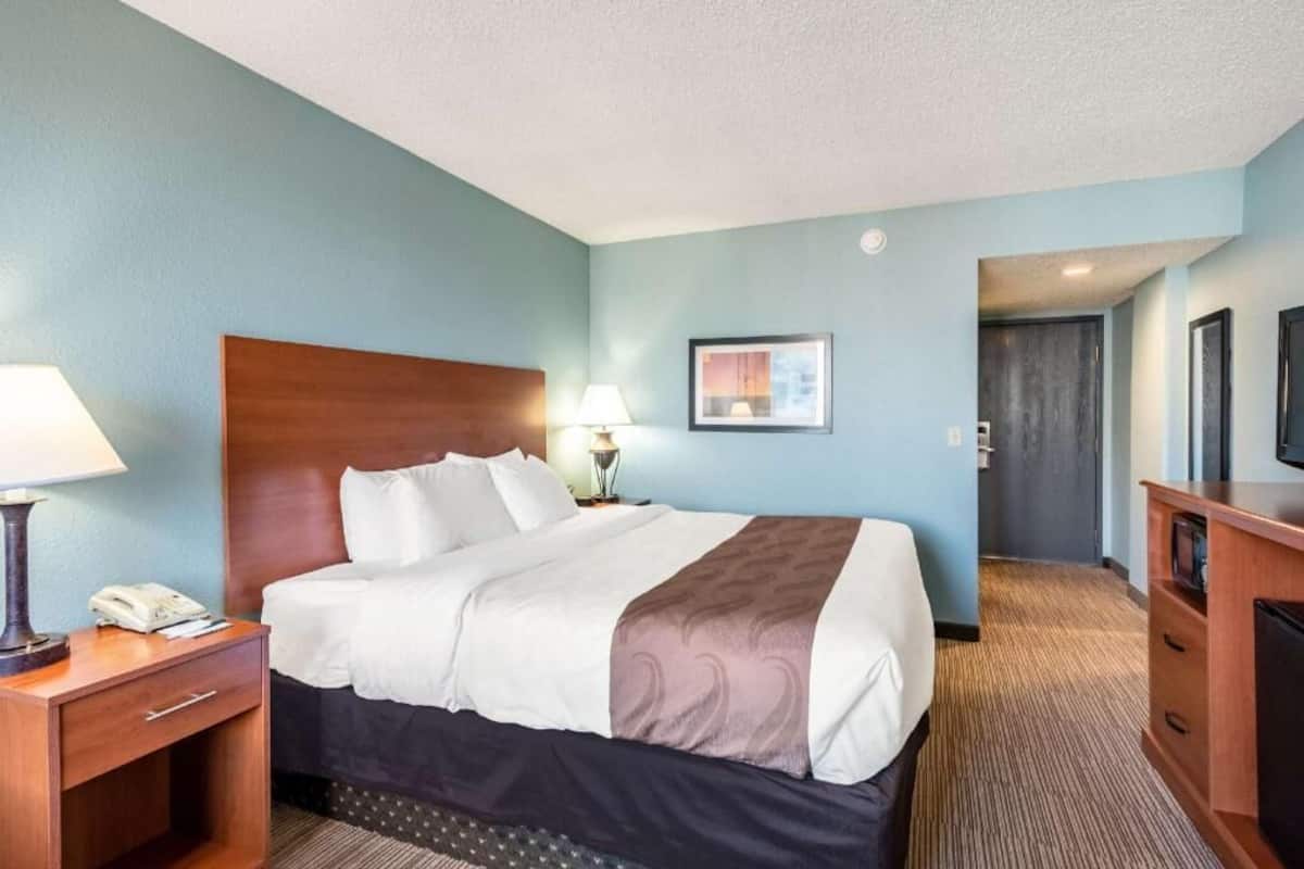 A hotel room with a bed, bedside tables, a lamp, a picture on the wall, and a television.