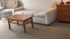 A hotel room with a sofa, a wooden coffee table, a chair, a lamp, a dresser, and a framed picture on the wall. - Quality Inn and Suites Garden of the Gods (Colorado Springs)