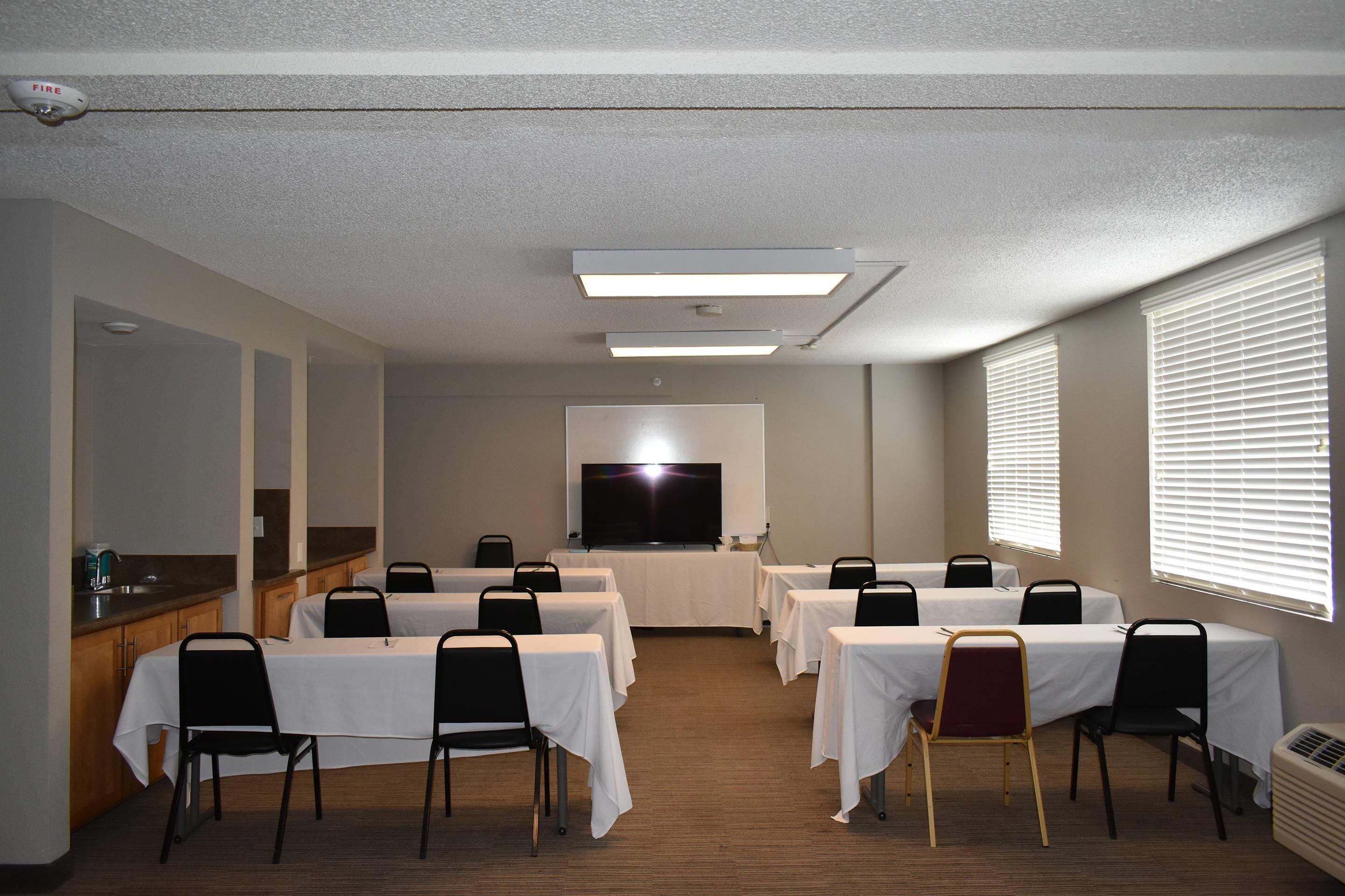 Une salle de conférence équipée de tables et de chaises, d’un téléviseur à écran plat et d’un coin cuisine.