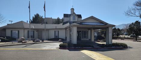 A two-story building with a covered entrance, a flagpole with the American flag, and a clear sky.