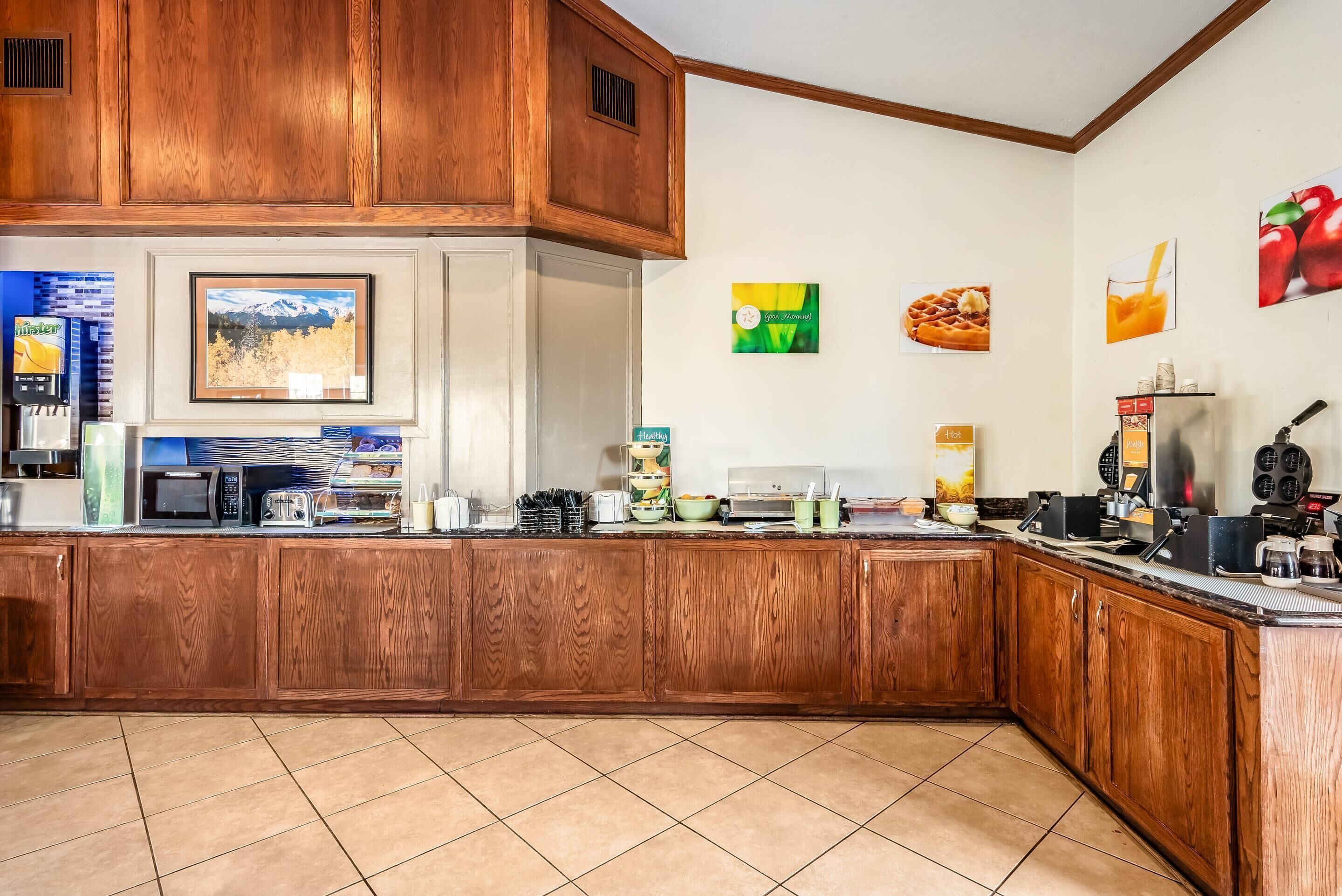A kitchen with wooden cabinets, a microwave, toaster, and various appliances. There are framed pictures on the wall and a coffee machine on the counter.