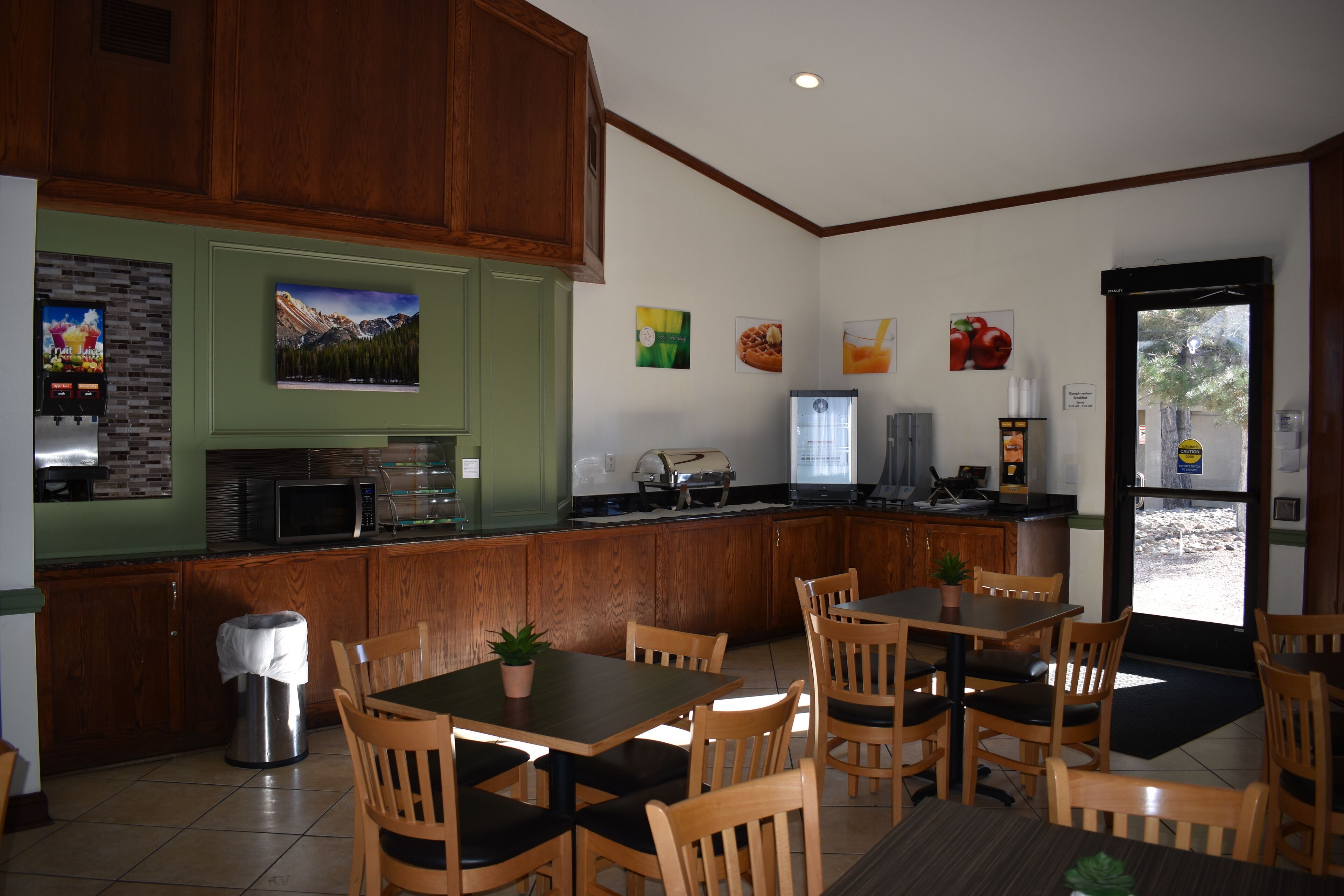 A restaurant with wooden furniture, a kitchen area, and a view through the door.