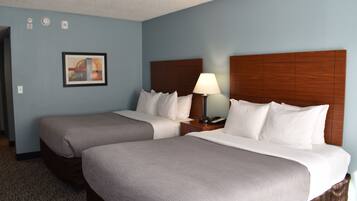 A hotel room with two beds, a nightstand with a lamp, a framed picture on the wall, and a carpeted floor.