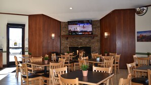 A restaurant with wooden tables and chairs, a TV mounted on a stone wall, and a fireplace. - Quality Inn and Suites Garden of the Gods (Colorado Springs)