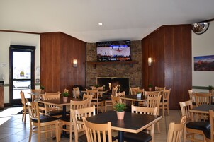 A restaurant with wooden tables and chairs, a TV mounted on a stone wall, and a fireplace.