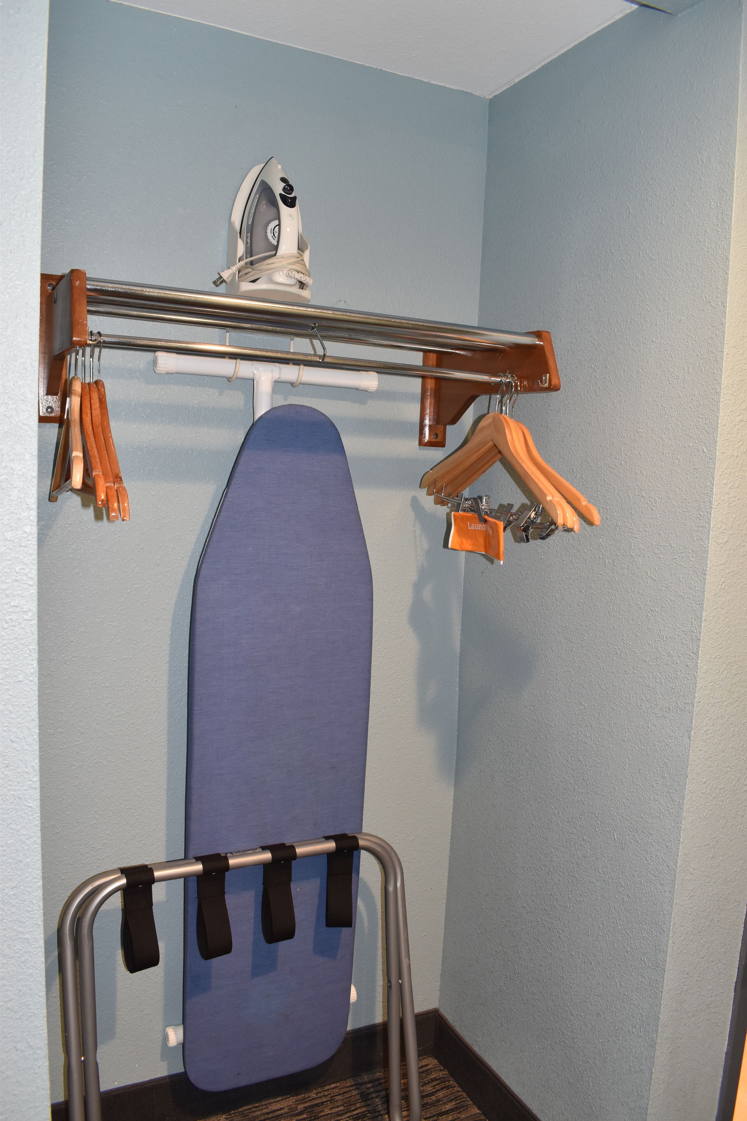 A hotel room with a blue ironing board, a hanging clothes rack, and a ceiling-mounted iron.
