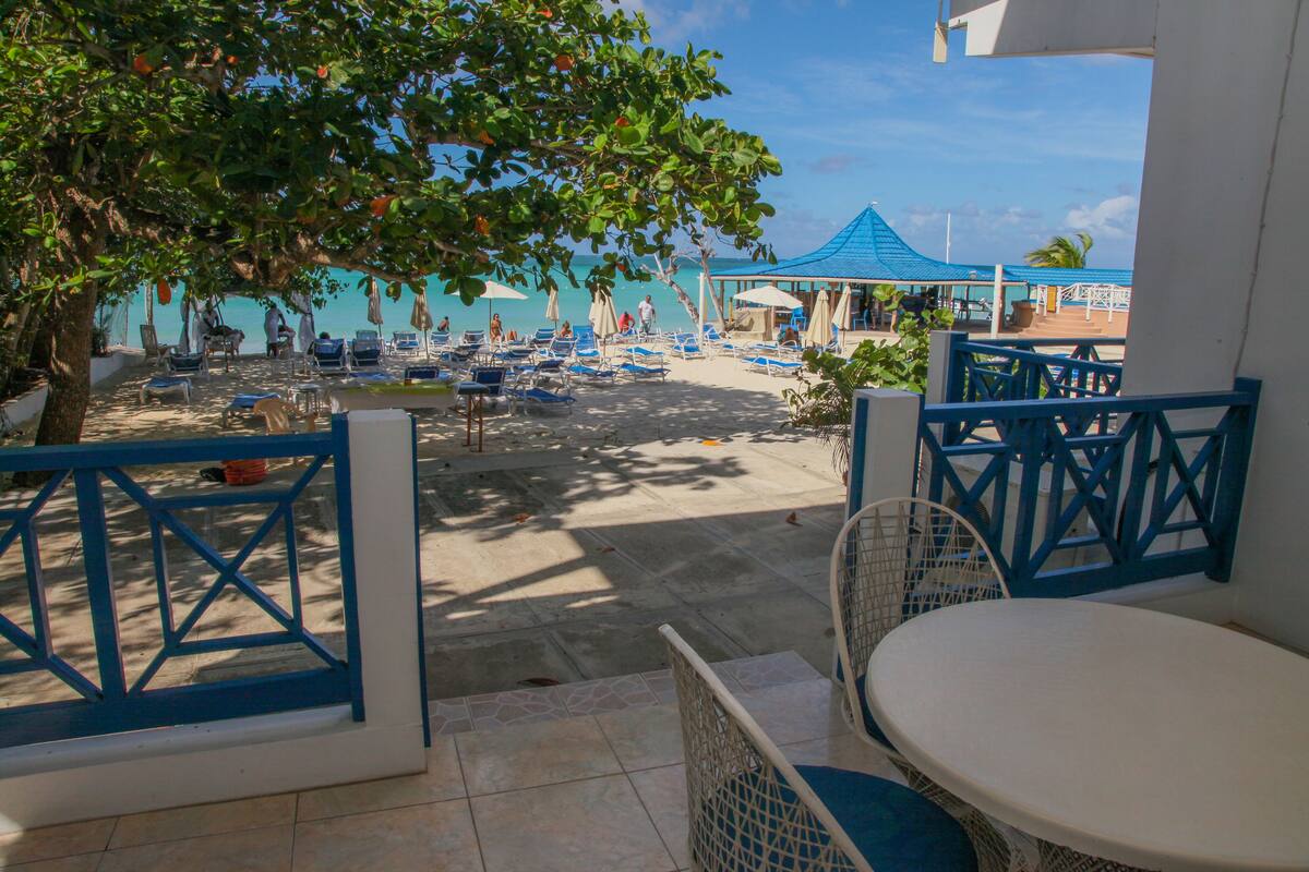 A beachside patio with blue and white furniture, a covered seating area, and a view of the ocean.