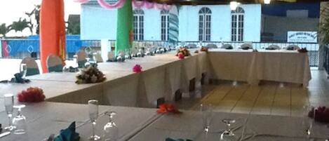 A banquet hall with tables set for a formal event, featuring a long table with chairs and a smaller table with a floral arrangement.