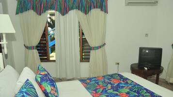 Quarto com cama, almofadas, cortinas, uma televisão e um ar condicionado.