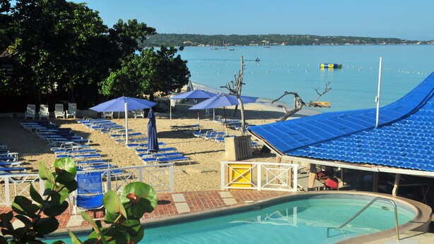 A poolside area with lounge chairs and umbrellas, a clear view of the sea, and a distant shoreline.