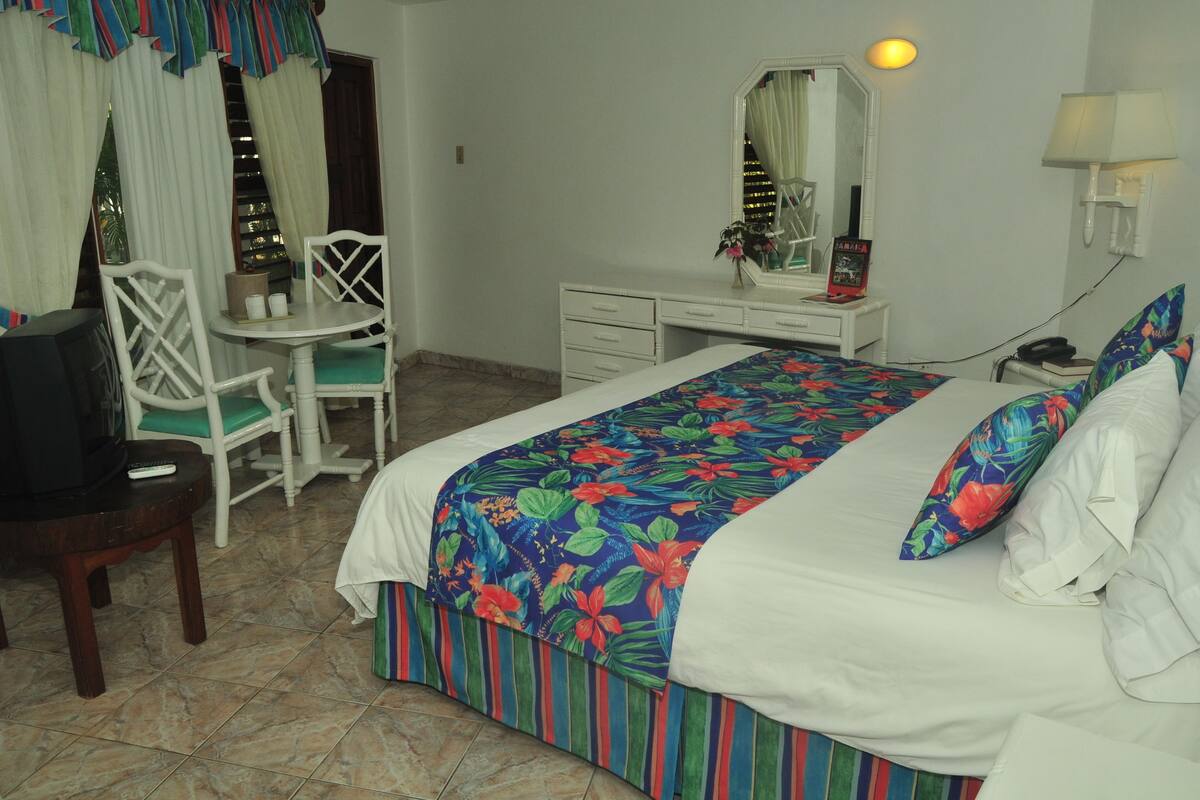 A hotel room with a bed, a desk, a chair, a television, and a mirror.
