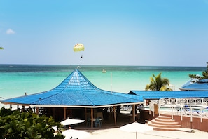 A beachside area with blue-roofed structures, a parasail in the distance, and a clear view of the ocean. - Negril Tree House Resort (Negril)