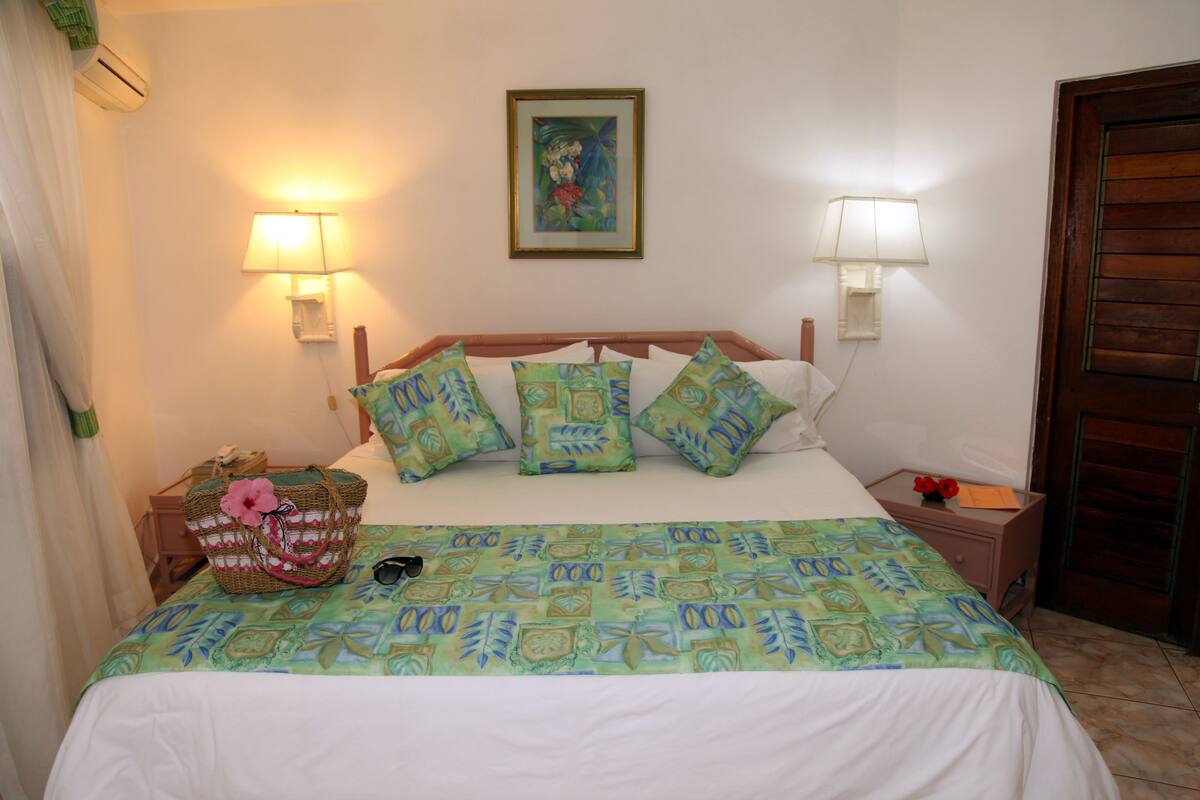 A neatly made bed with a patterned bedspread, two wall-mounted lamps, a framed picture above the bed, and a wooden door to the right.