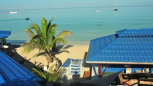 A beach view with a clear sky, a palm tree, and a boat in the distance.