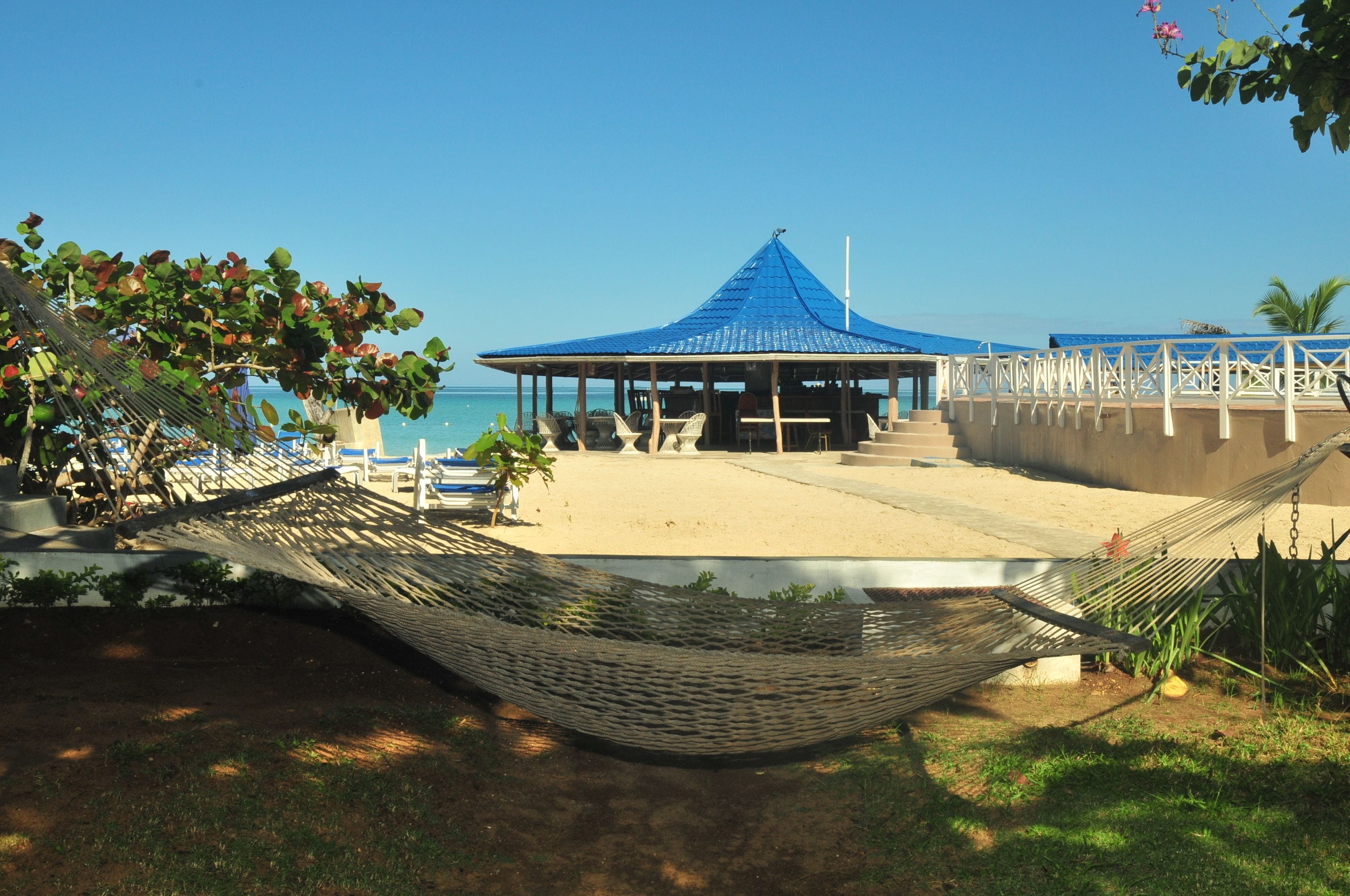 A beachside gazebo with a blue roof, surrounded by lounge chairs and a hammock.