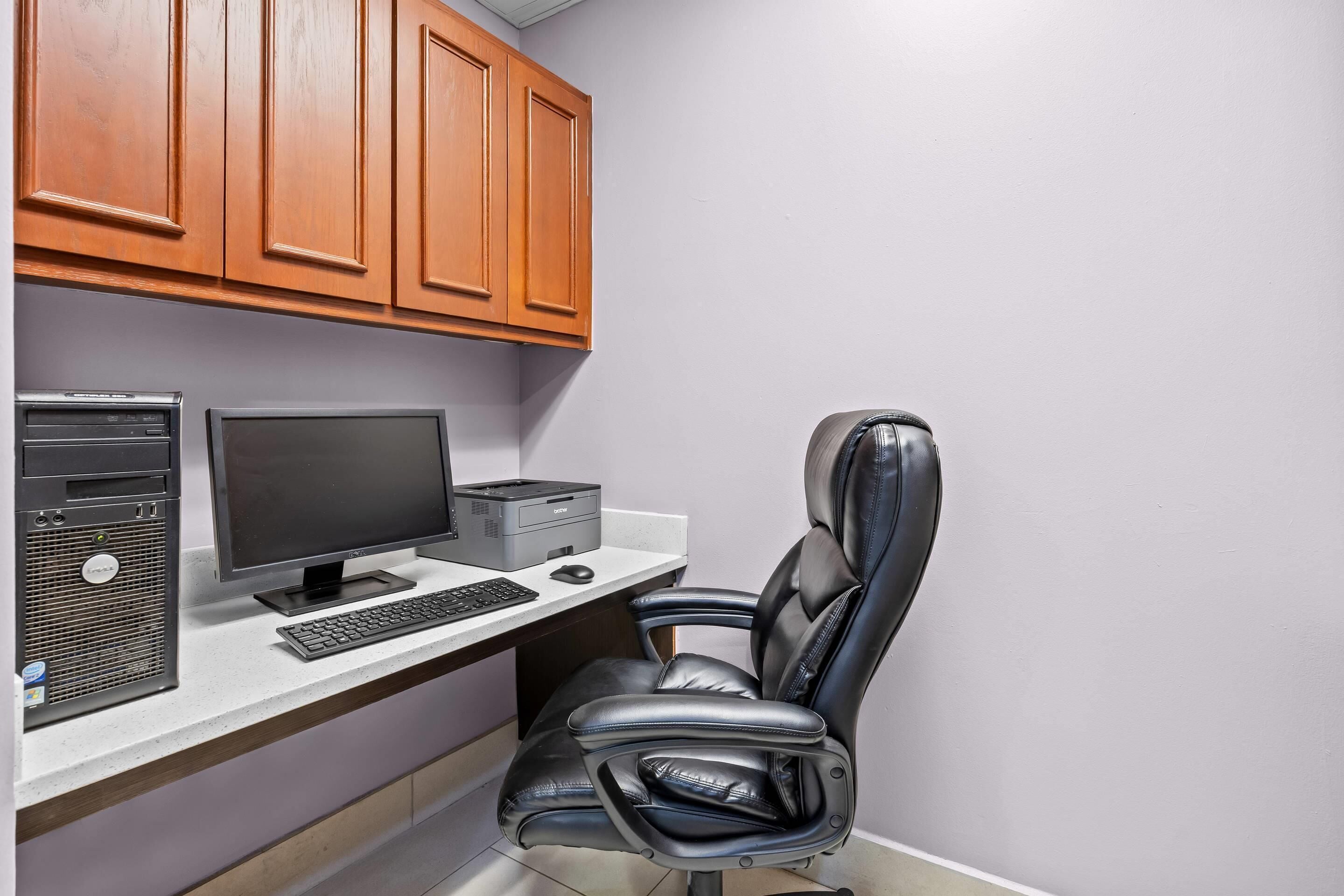 A home office setup with a desktop computer, monitor, keyboard, and a leather office chair.