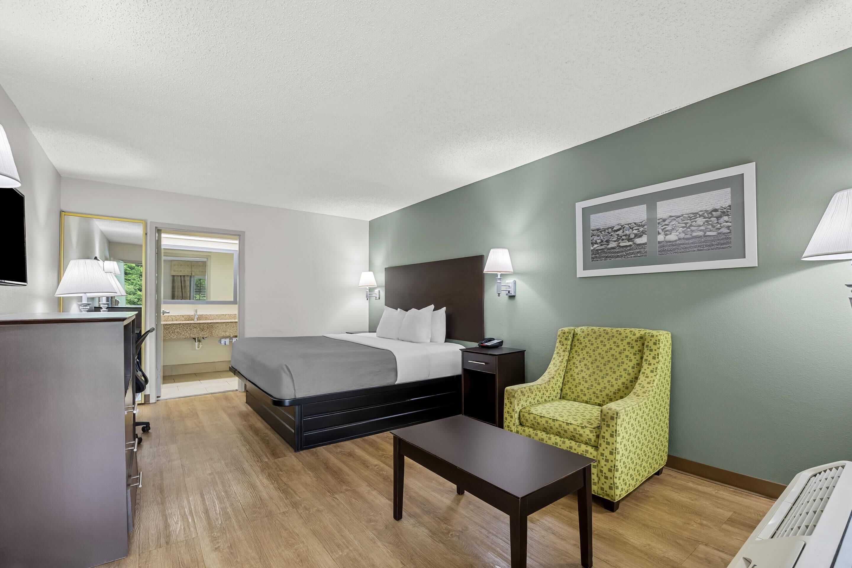 Une chambre d’hôtel comprenant un lit, une table de chevet, une chaise et un tableau accroché au mur.