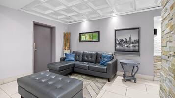 A modern living room with a sectional sofa, a matching ottoman, a small side table, and a cityscape painting.