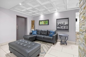 Una sala de estar moderna con un sofá seccional, un reposapiés a juego, una mesita auxiliar y una pintura de un paisaje urbano.