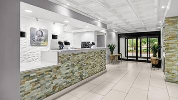 Zona de recepción de un hotel con diseño moderno, que incluye un mostrador de recepción, una pantalla digital y un cartel que dice 'Quality by Choice Hotels'.