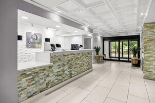 Zona de recepción de un hotel con diseño moderno, que incluye un mostrador de recepción, una pantalla digital y un cartel que dice 'Quality by Choice Hotels'.