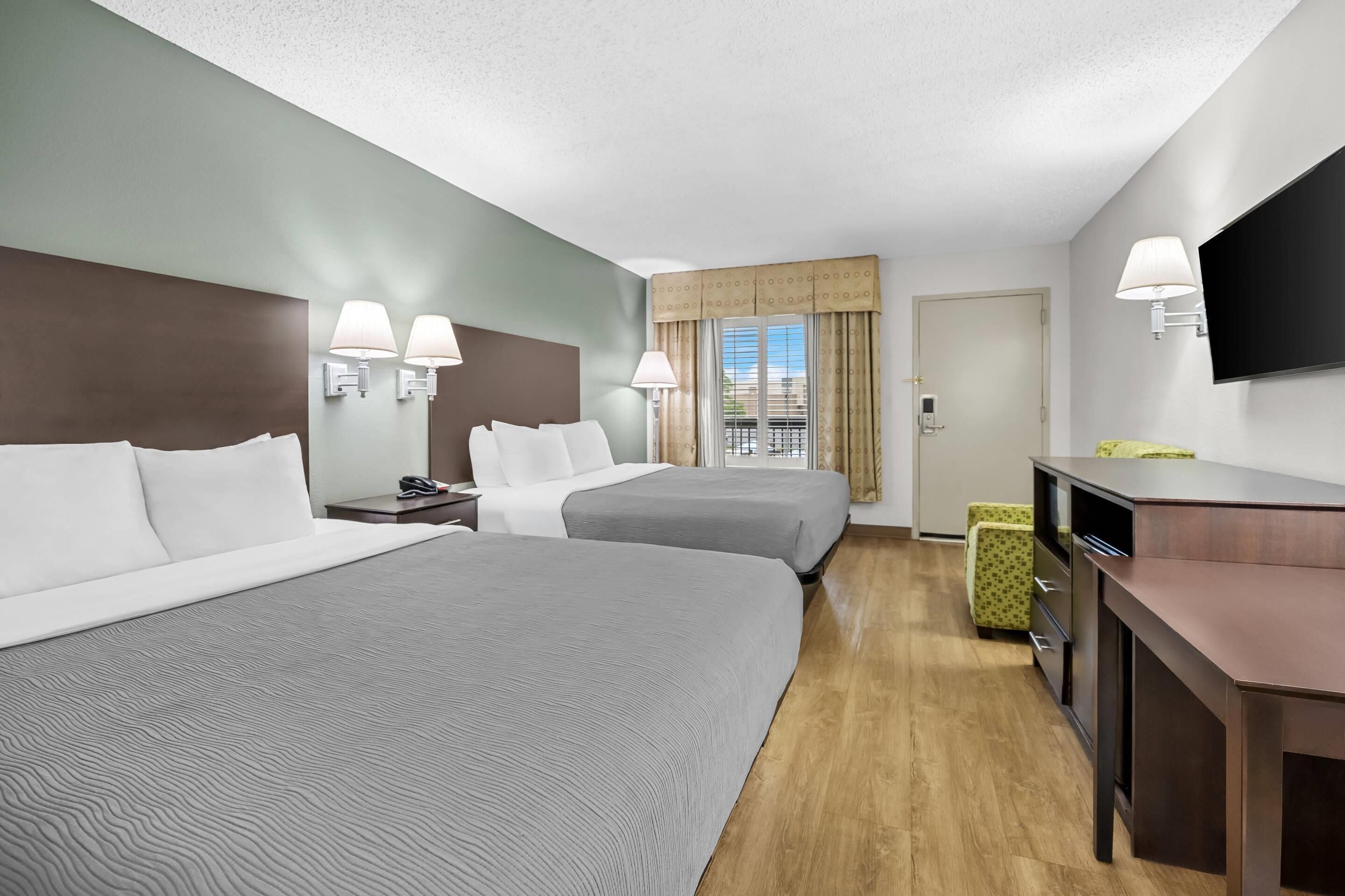 A hotel room with two beds, a desk, a TV, and a window with curtains.