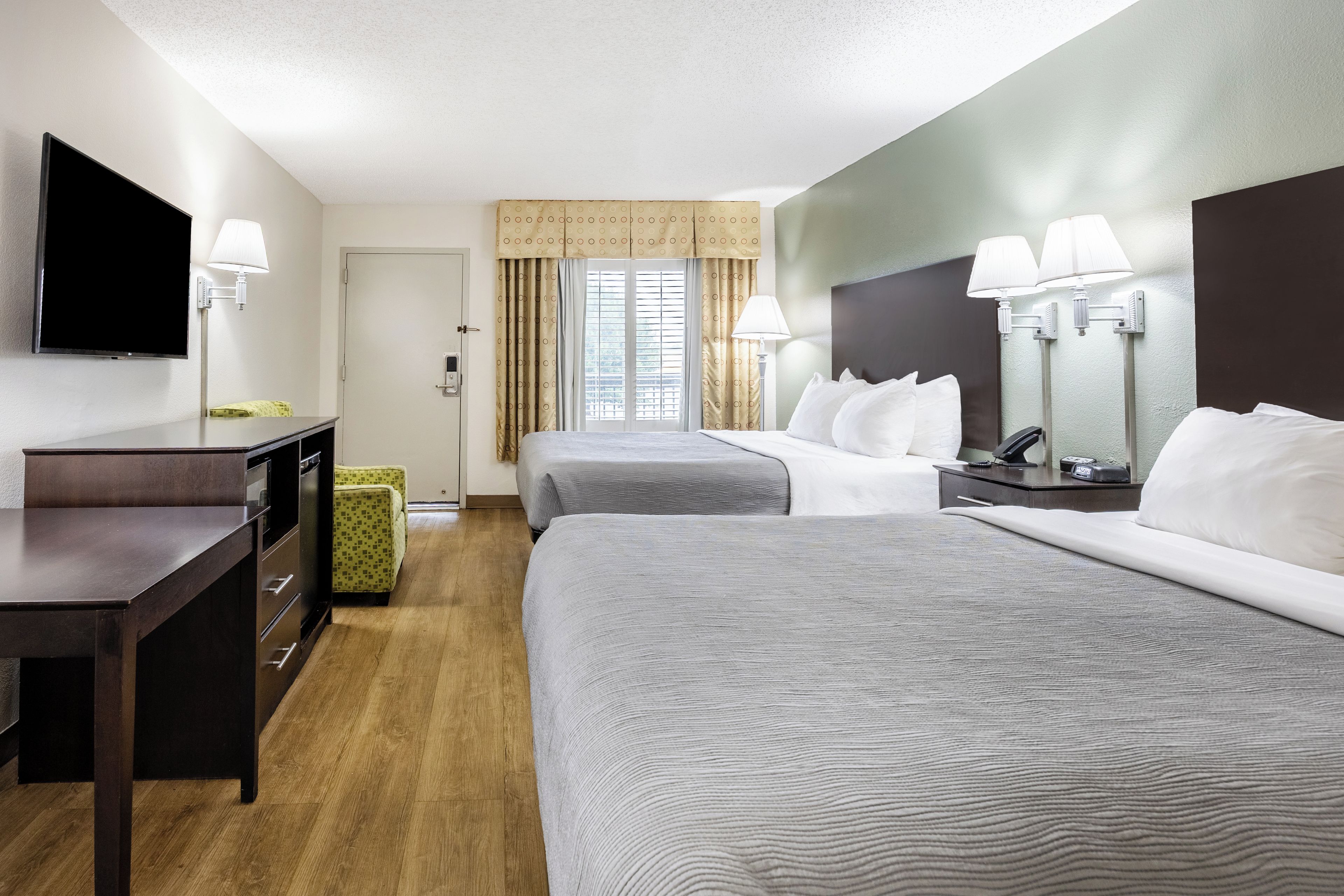 Habitación de hotel con dos camas, un escritorio, un televisor y una ventana con cortinas.