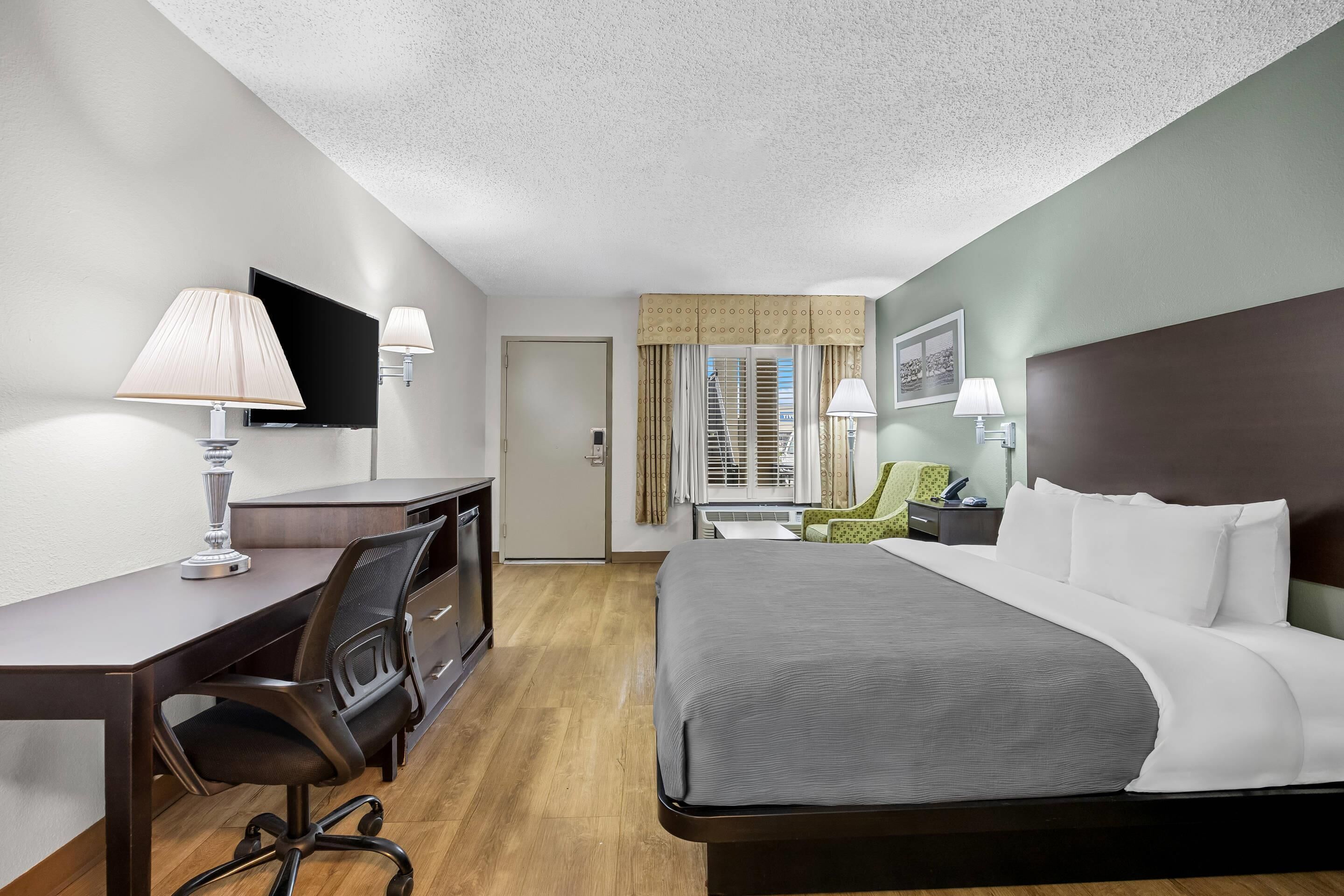 A hotel room with a bed, desk, chair, TV, and a window with curtains.