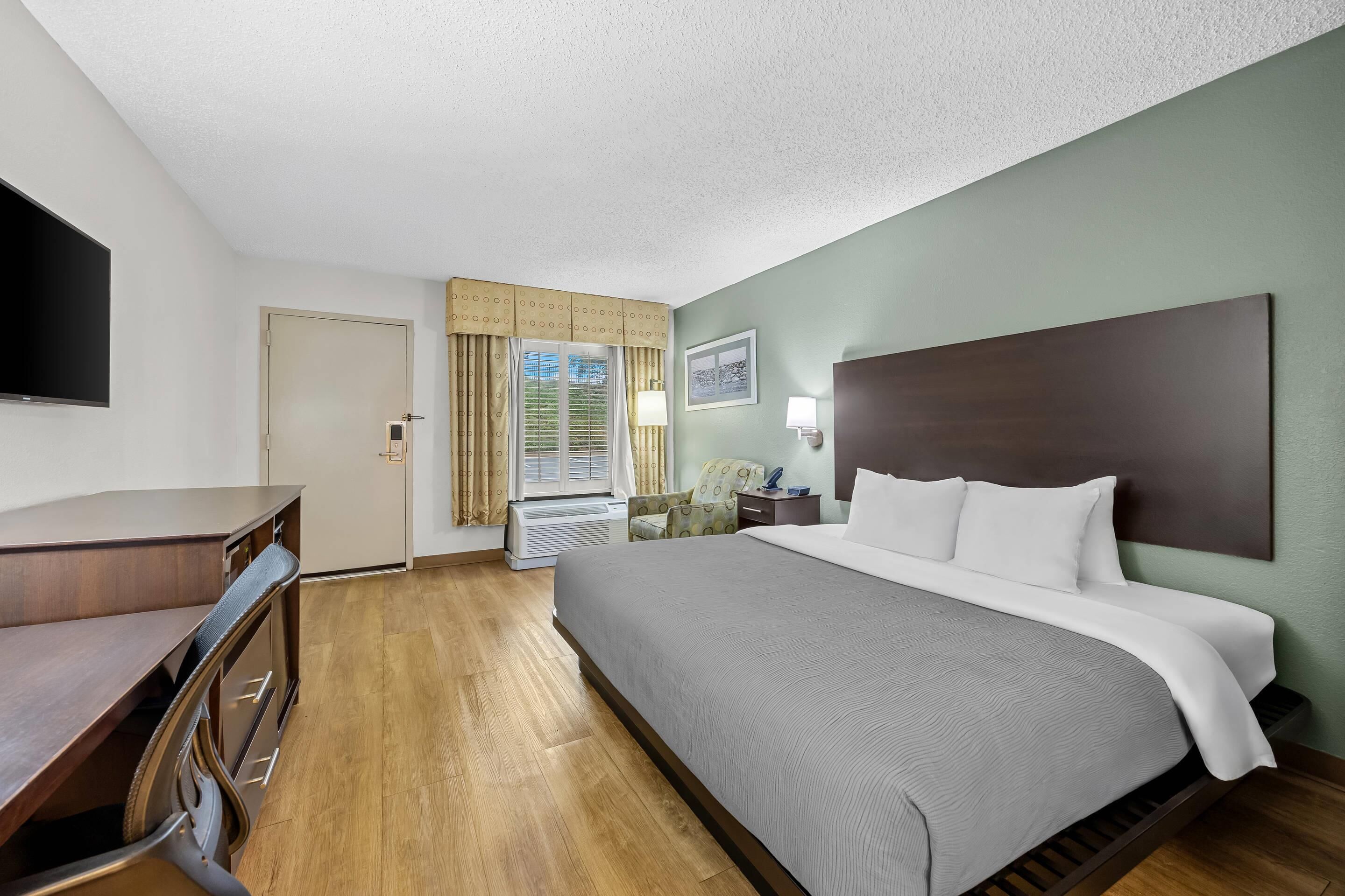 Une chambre d’hôtel avec un lit, un bureau, une chaise, une télévision et une fenêtre avec des rideaux.