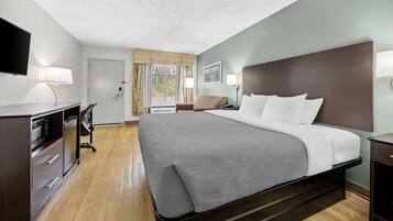 A hotel room with a bed, a desk, a chair, a TV, and a window with curtains.