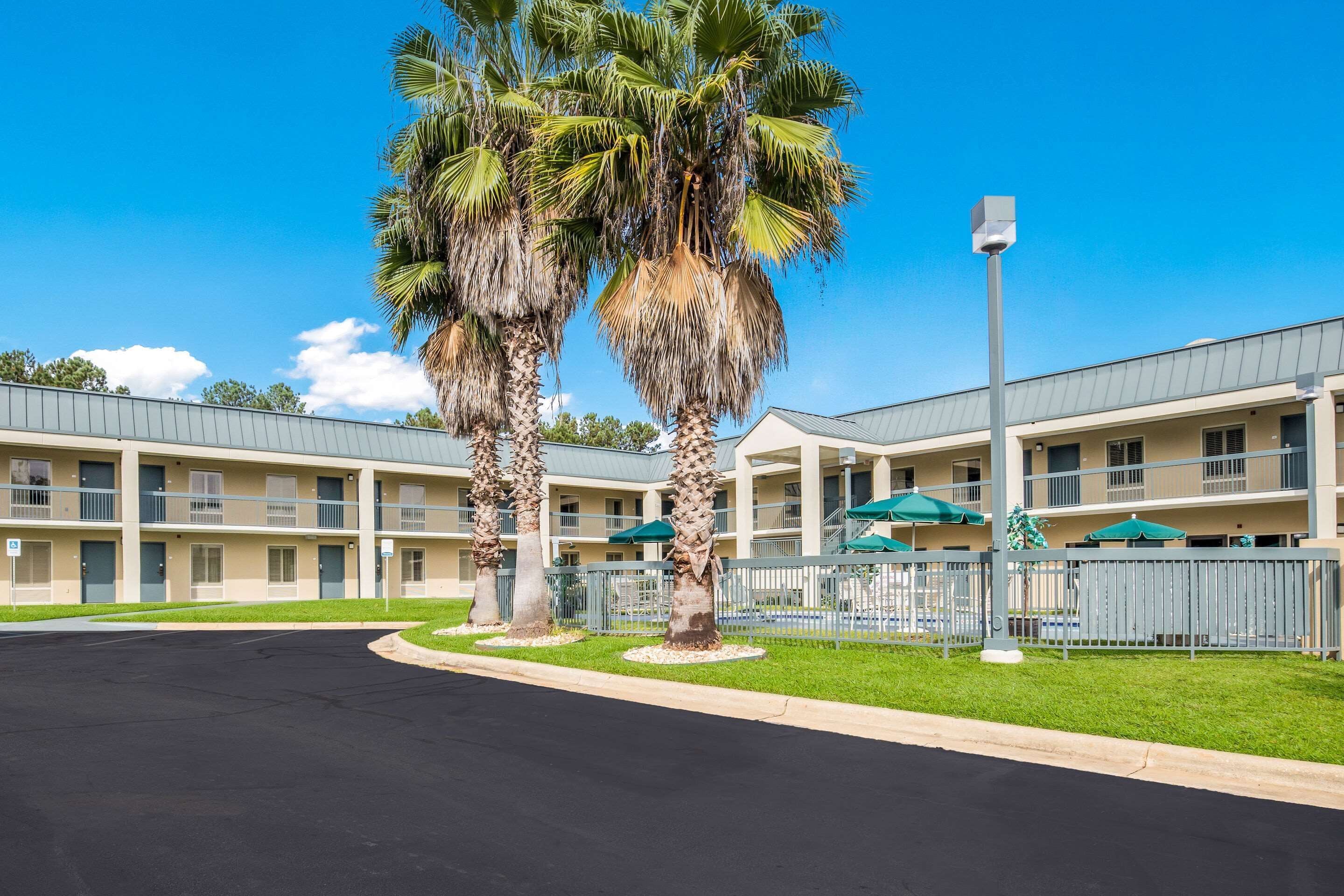 A multi-story hotel with a flat roof, a parking lot, and palm trees in front.