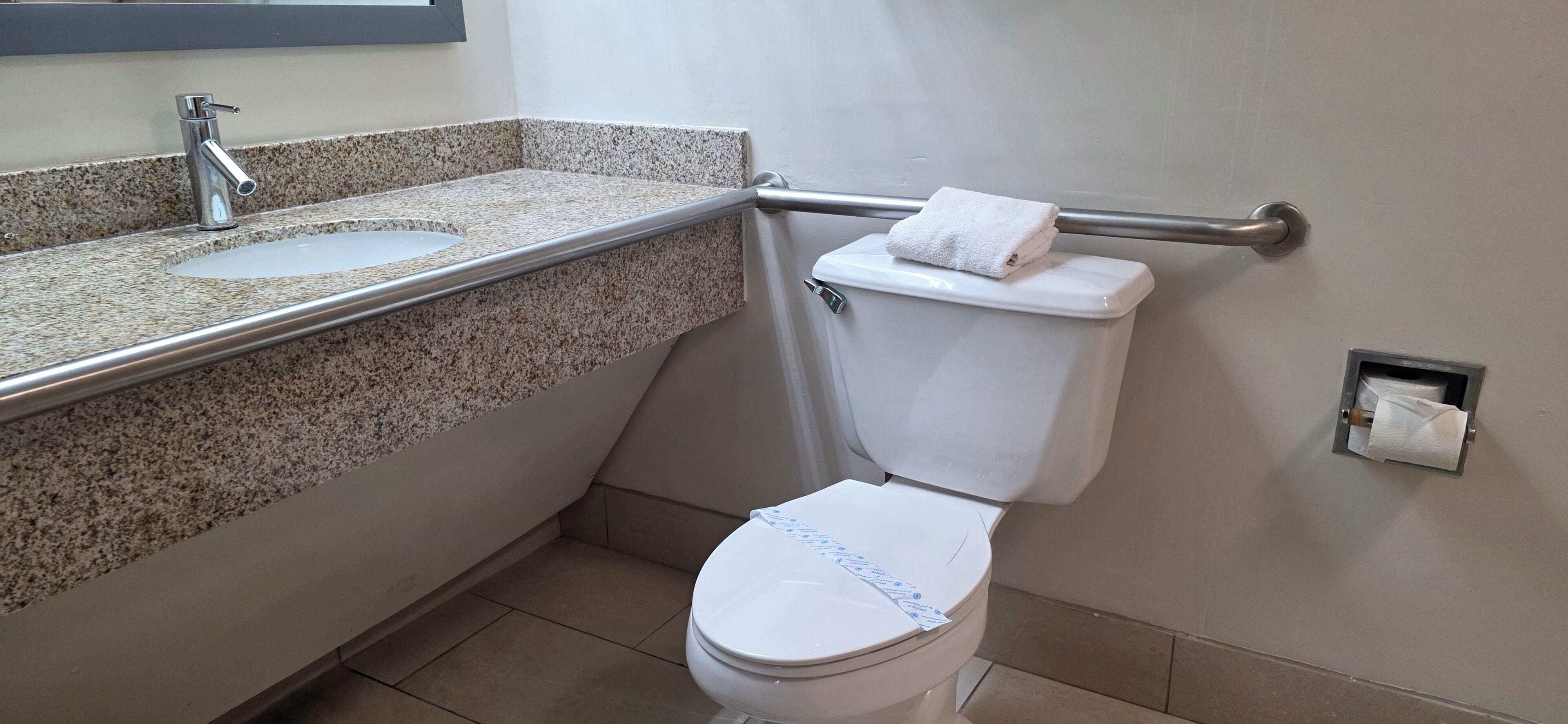 A bathroom with a granite countertop sink, a toilet, and a towel rack.