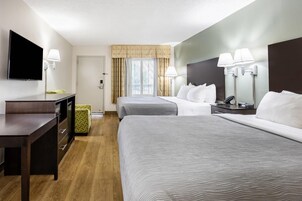 Habitación de hotel con dos camas, un escritorio, un televisor y una ventana con cortinas.