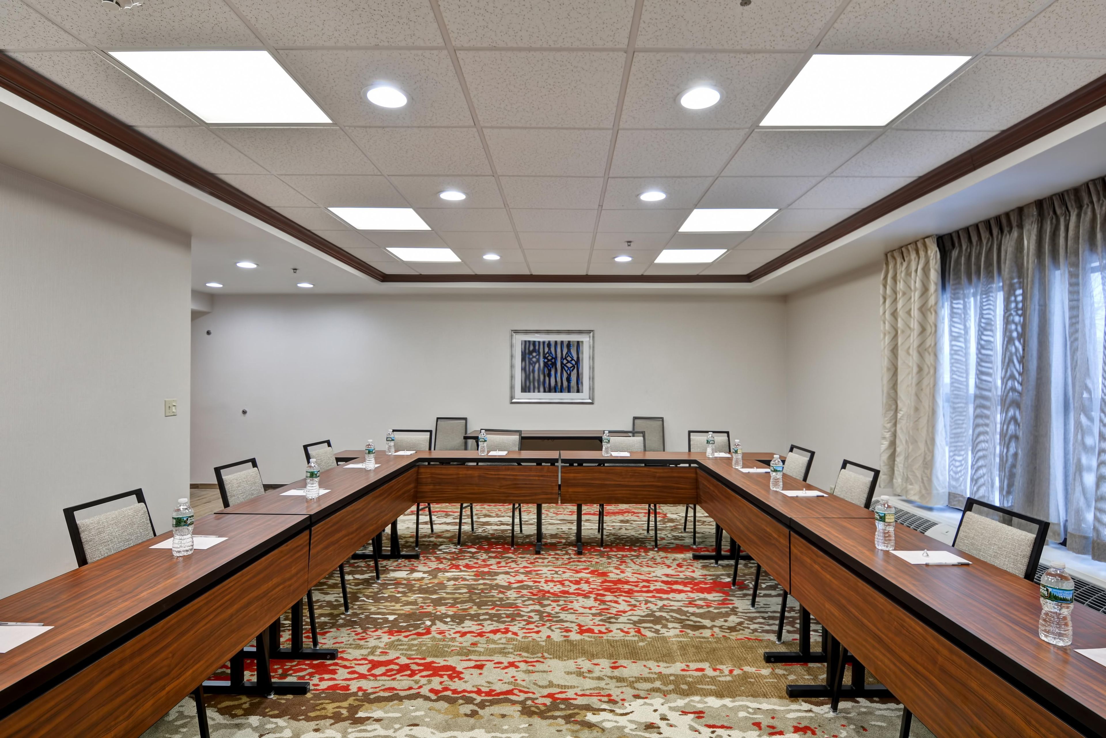 A conference room with a long table, chairs, water bottles, and a patterned carpet.