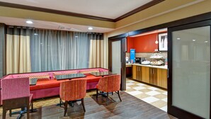 A hotel room with a sofa, chairs, a dining table, and a kitchen area with a checkered floor. - Hampton Inn Albany-Wolf Road (Airport) (Albany)