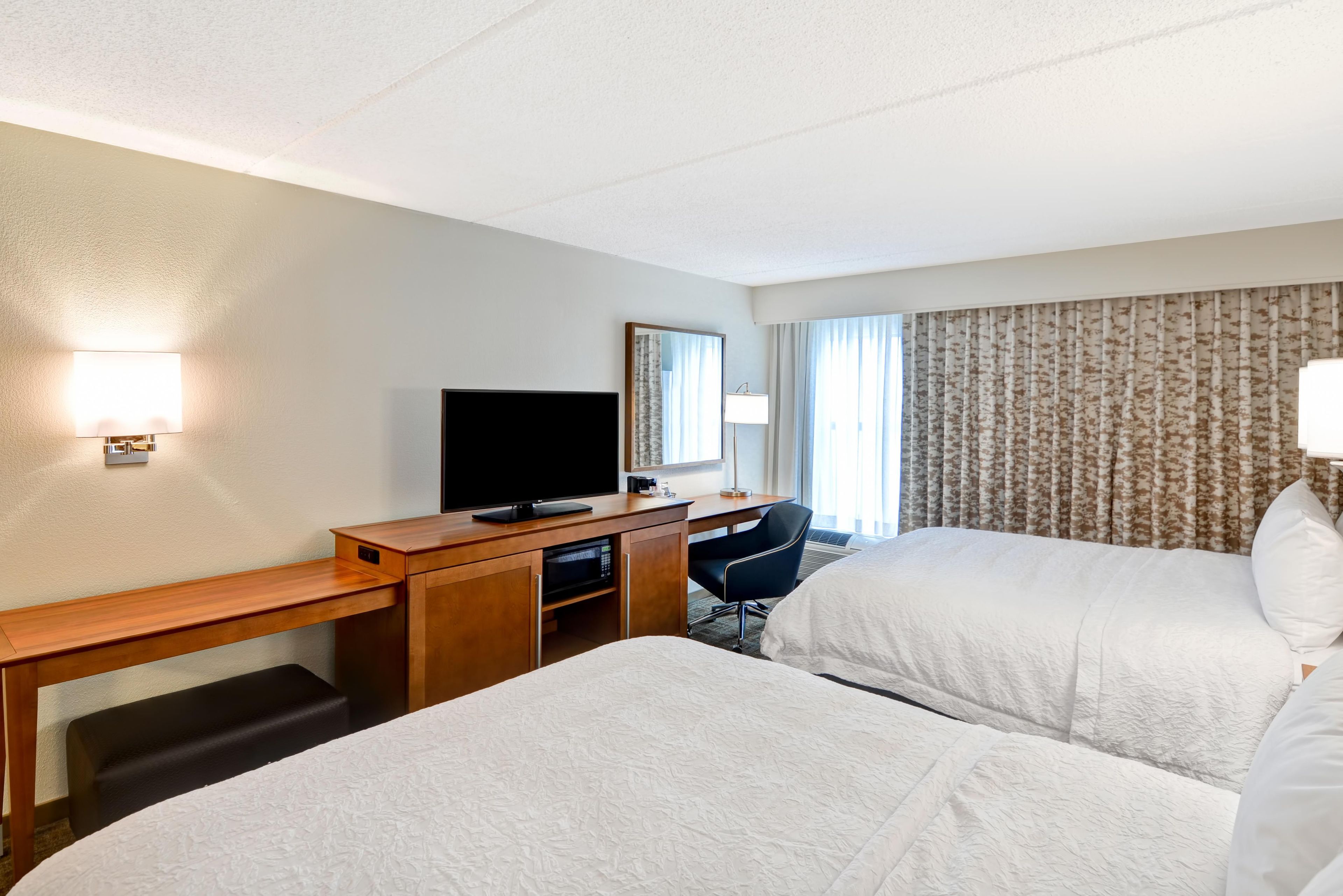 Habitación de hotel con cama, escritorio con televisor, silla y ventana con cortinas.