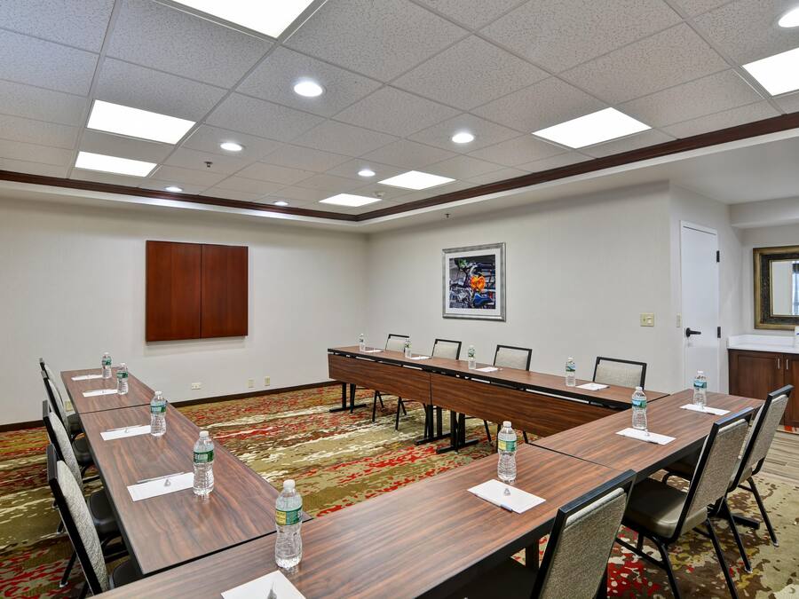 Uma sala de conferências com uma mesa comprida, cadeiras, garrafas de água e um quadro pendurado na parede.