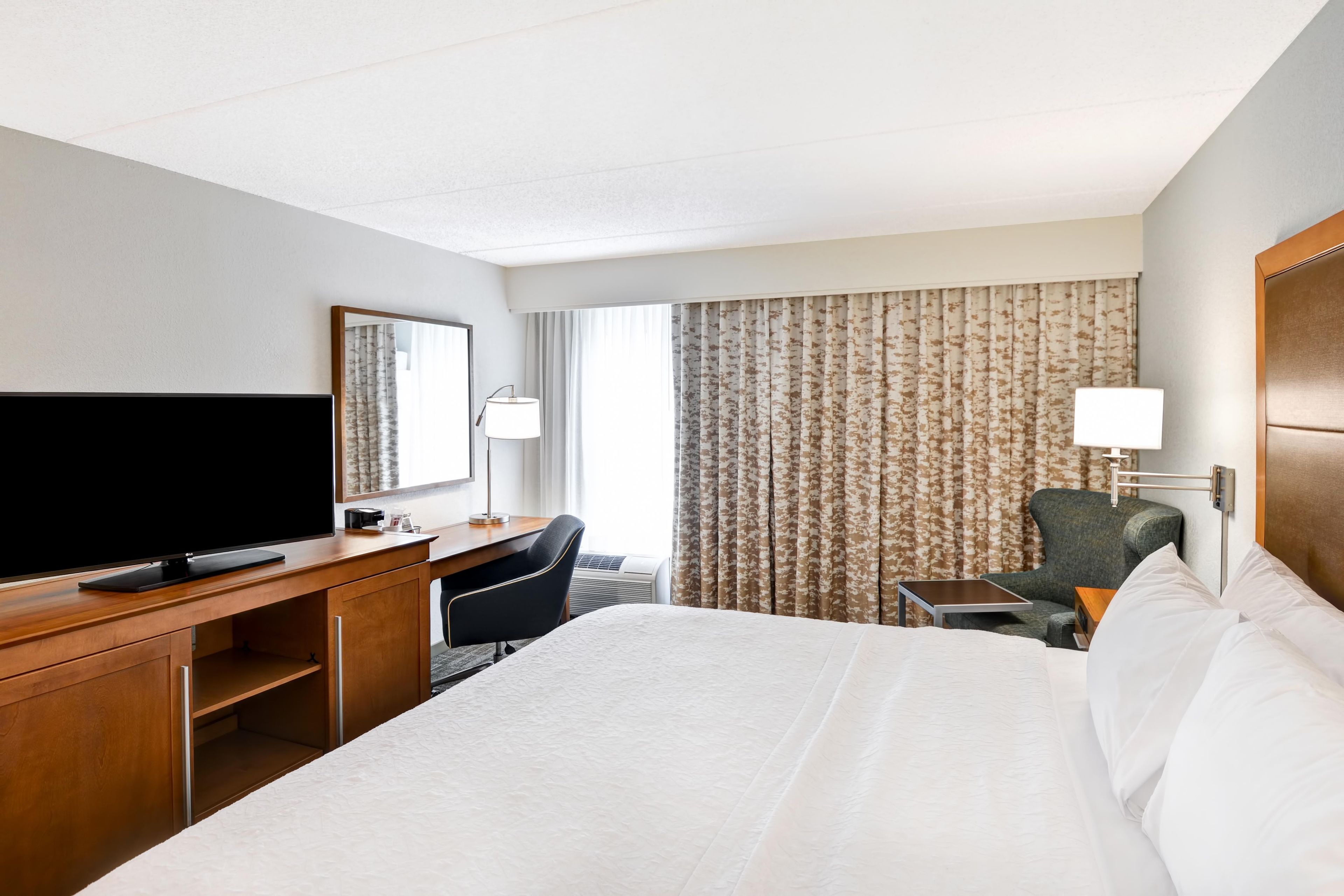 Une chambre d’hôtel avec un grand lit, un bureau doté d’un téléviseur à écran plat, une chaise, une petite table et une lampe.