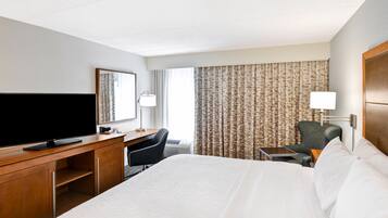 Une chambre d’hôtel avec un grand lit, un bureau doté d’un téléviseur à écran plat, une chaise, une petite table et une lampe.