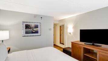 Habitación de hotel con una cama, un televisor sobre un soporte de madera, un cuadro en la pared y una mesita de noche con una lámpara.