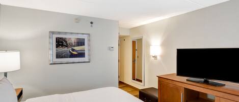 Ein Hotelzimmer mit einem Bett, einem Fernseher auf einem Holztischchen, einem gerahmten Bild an der Wand und einem Nachttisch mit einer Lampe.