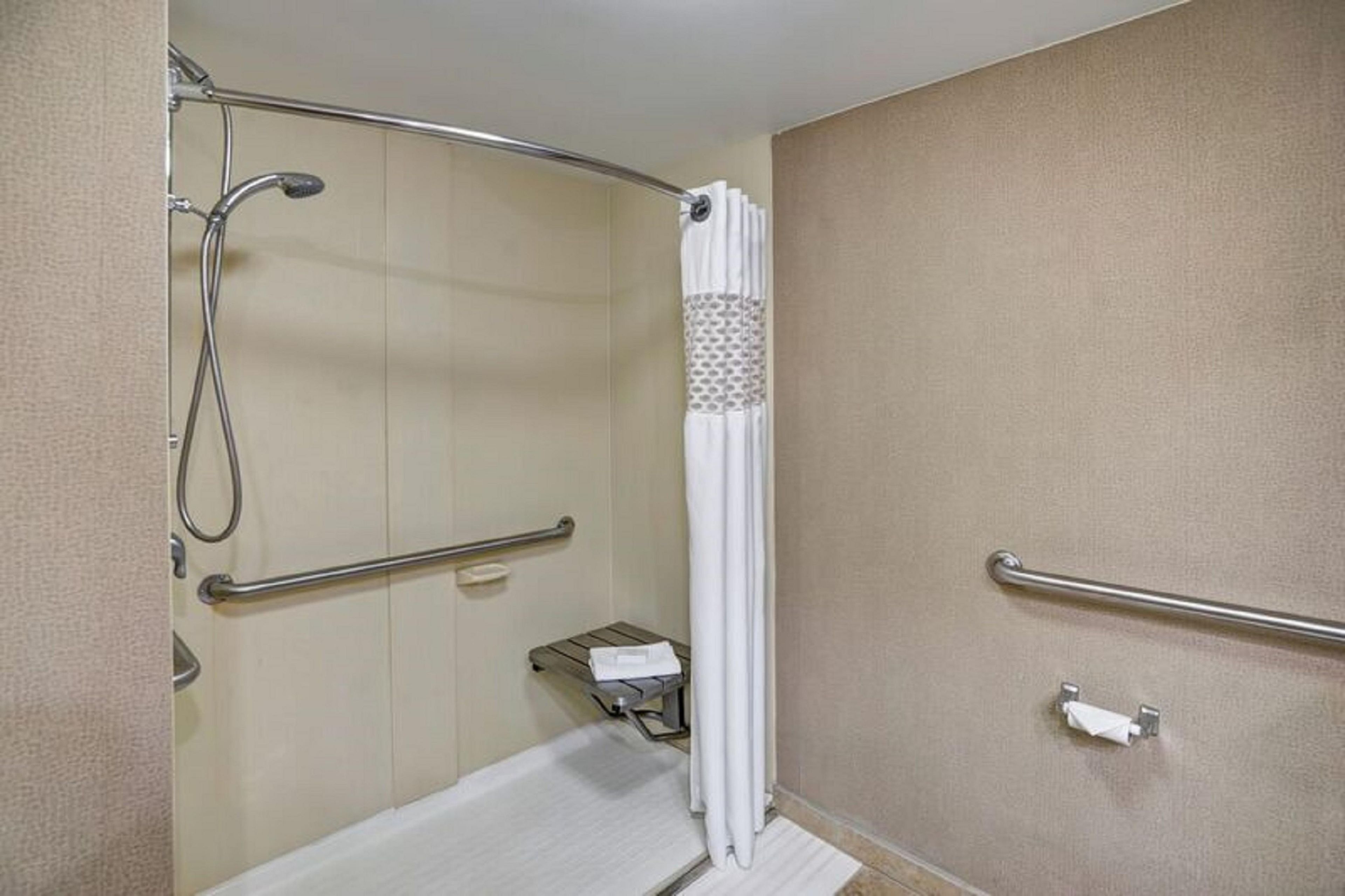 A bathroom with a shower, grab bars, a towel rack, and a toilet.